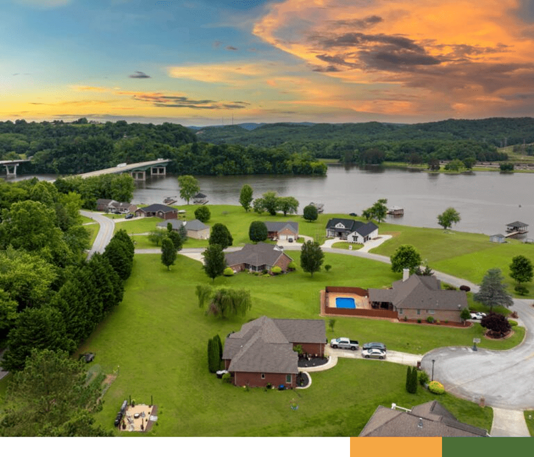 A scenic lakeside neighborhood at sunset with houses and greenery.