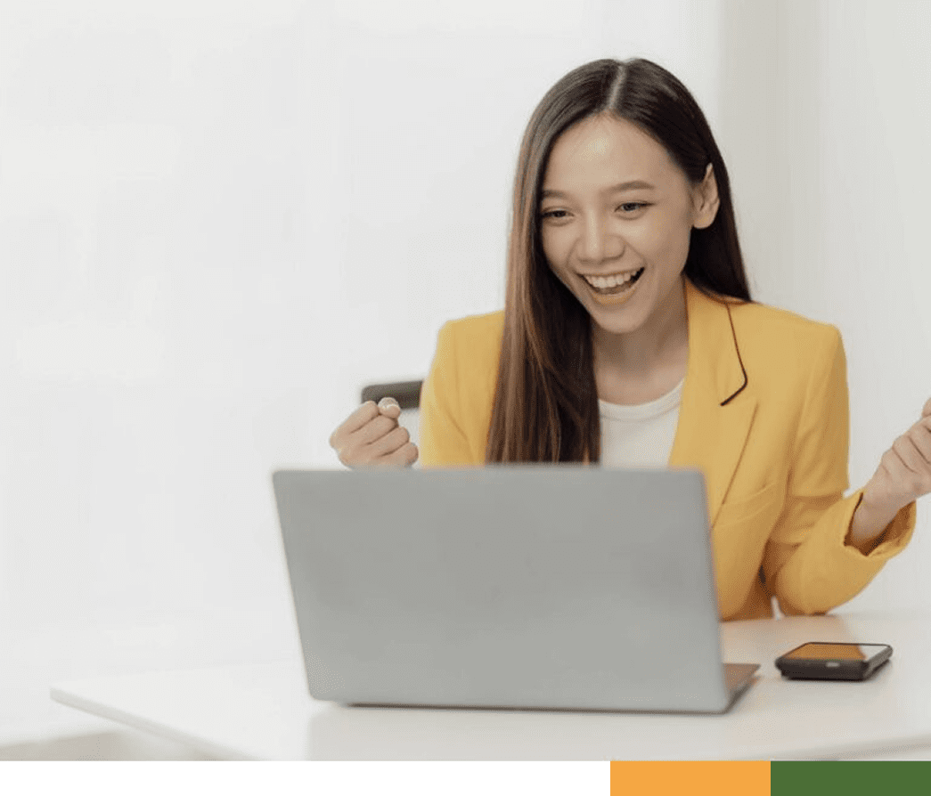 A woman happily using a laptop while eating with chopsticks.