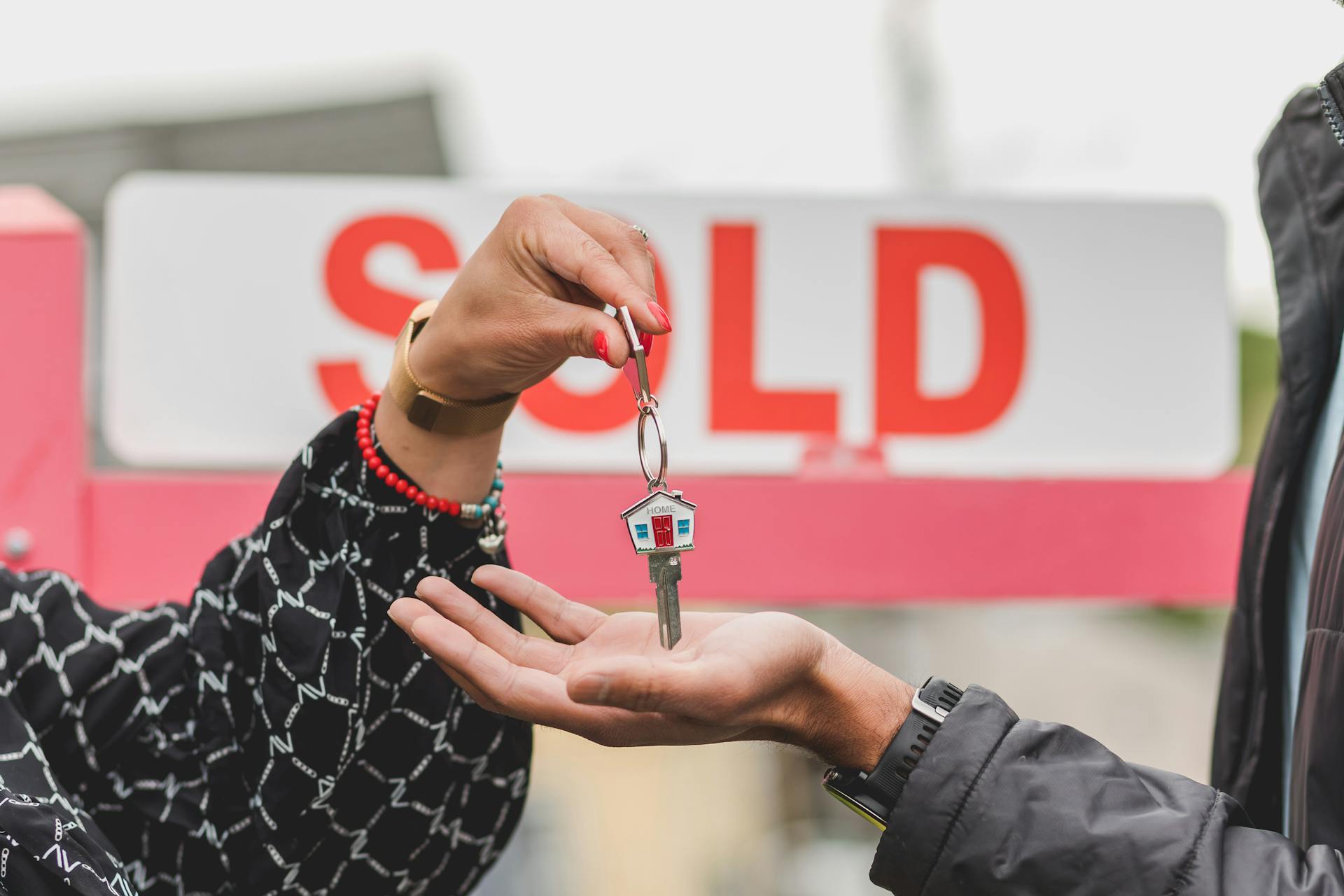 Hands exchanging house keys with a 'SOLD' sign in the background.