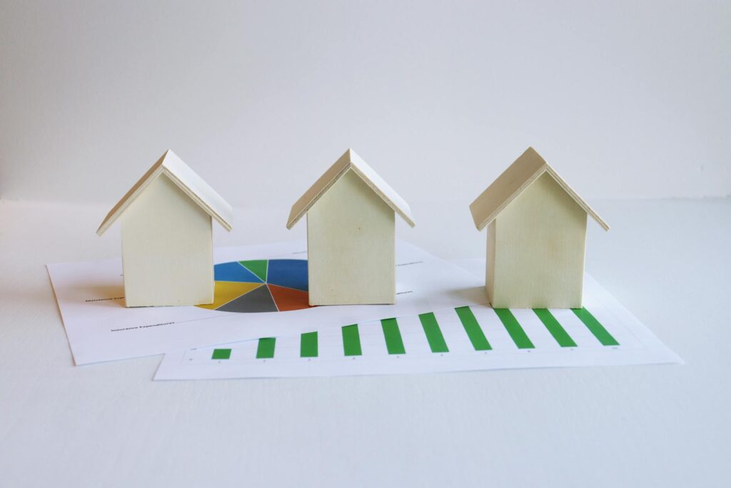 Three wooden house models in a row with a colorful credit card and green bar charts.